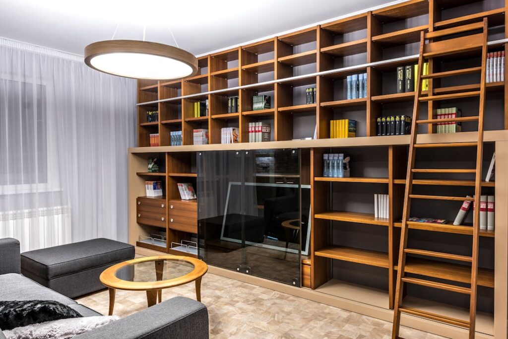 An image of a home library with a ladder and books on a shelf in front of a grey sofa