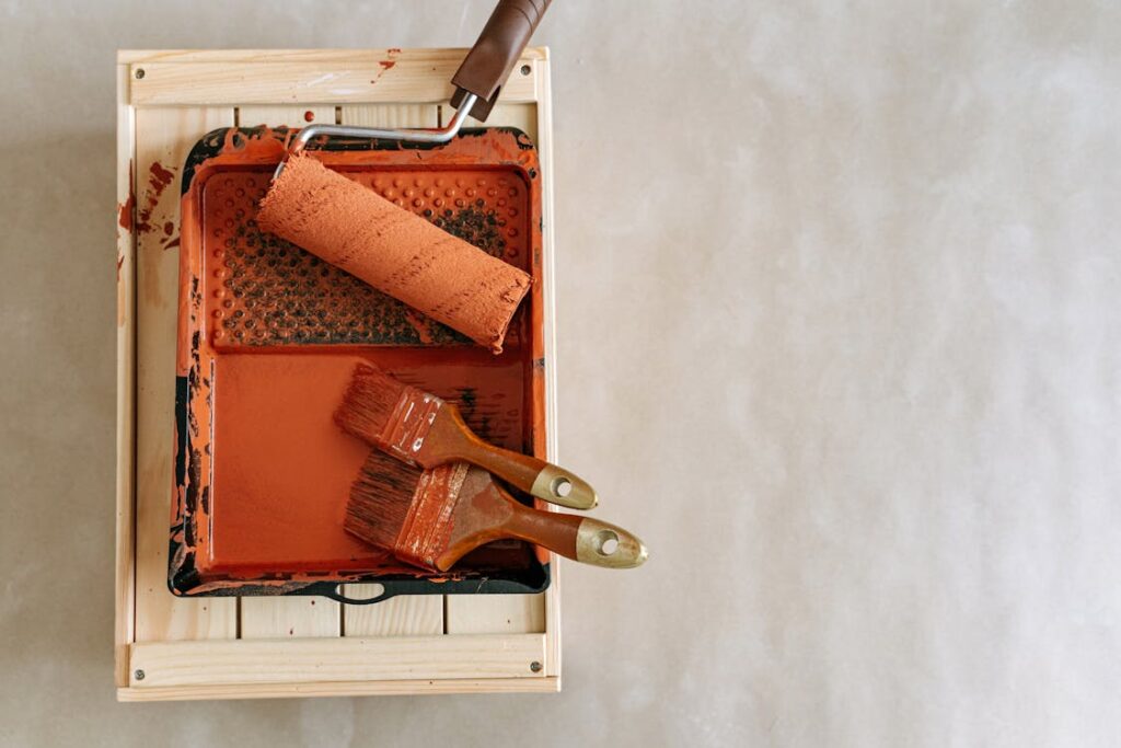 An image of a paintbrush and roller covered in red paint